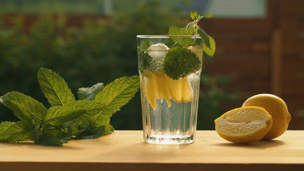 Sluit tonic soda fonkelend water met citroen, munt en ijs in een glas op de tafel in de tuin. Verfrissende frisdrank. Zomer stilleven - Foto, afbeelding