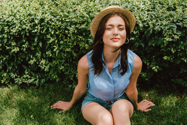 joyeuse jeune femme en chapeau de paille assis sur l'herbe - Photo, image
