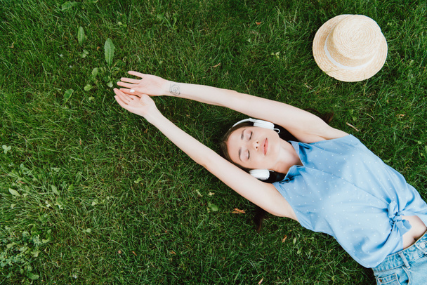 vista superior de la atractiva mujer acostada en la hierba y escuchar música cerca de sombrero de paja
 - Foto, Imagen