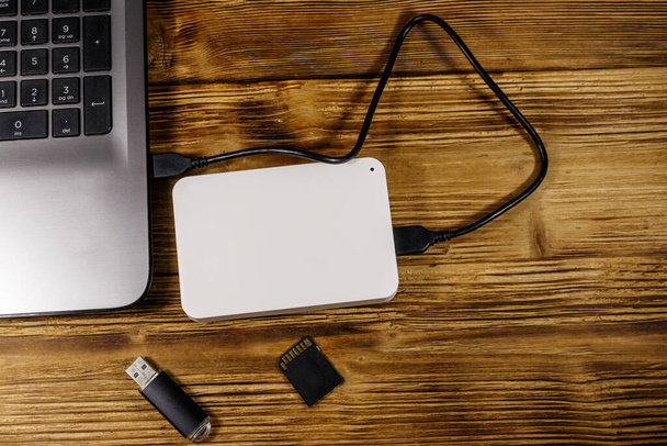 Zewnętrzny dysk twardy podłączony do laptopa, karty pamięci SD i pendrive 'a na drewnianym biurku. Widok góry. Pojęcie przechowywania danych - Zdjęcie, obraz