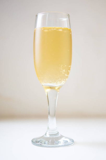 A glass of white sparkling wine. Champagne on the white table. Drink close-up. Gas bubbles in an alcoholic drink. - Photo, image