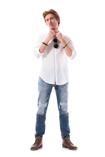 Vooraanzicht van een zelfverzekerde jonge knappe man die een wit shirt aantrekt en zich klaarmaakt. Volledige lichaamslengte geïsoleerd op witte achtergrond.  - Foto, afbeelding