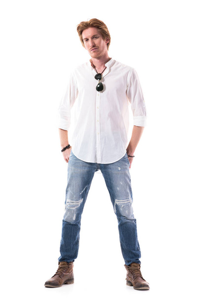Modelo de moda masculina de moda en jeans azules y botas de cuero posando con las manos en los bolsillos traseros. Longitud total del cuerpo aislado sobre fondo blanco
.  - Foto, Imagen