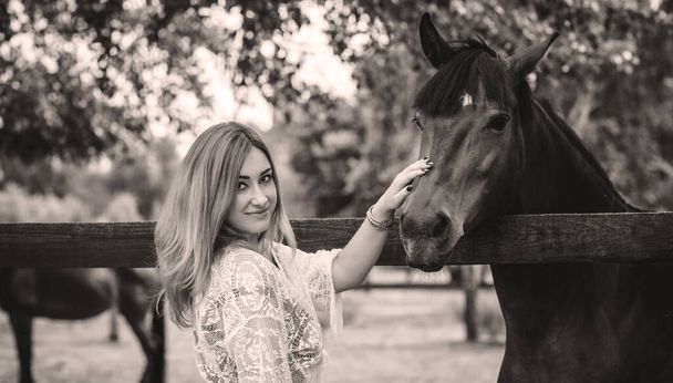 Woman in fashionable Bohemian casual style with horses on a farm, pets animals in village at rancho. Horses are human friends - Foto, Bild