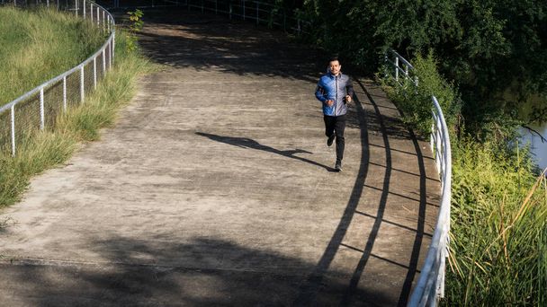 Ein Mann im Kapuzenpullover joggt abends nach anstrengender Arbeit im Stadtpark. Lauftraining und Krafttraining im Freien in der Waldstadt. Archivbild - Foto, Bild