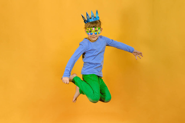 A boy in a cardboard crown is jumping on an orange background. - Fotoğraf, Görsel