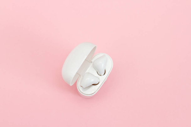 Wireless headphones in case on a pink background. - Foto, afbeelding