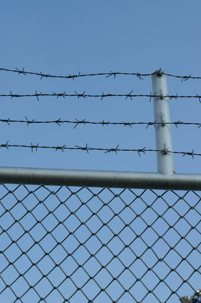 Забор из колючей проволоки и голубое небо - Фото, изображение