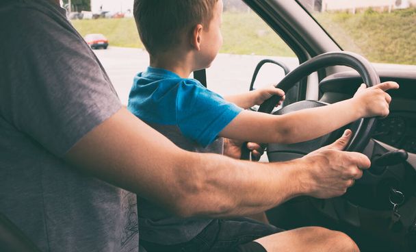 The child is sitting on the father's knees in the car and learning how to drive the car - Фото, зображення