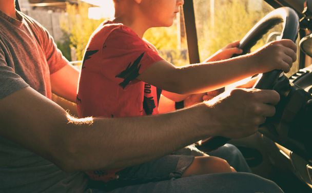 The child is sitting on the father's knees in the car and learning how to drive the car - 写真・画像