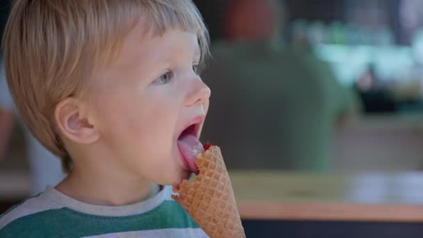Eis, kleiner attraktiver Junge leckt sich gerne die Zunge im sommerlich kühlen Dessert-Eis im Waffelbecher - Filmmaterial, Video