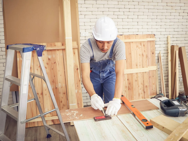 Азиатский молодой плотник или ремонтник в белом шлеме. Работа с деревом в помещении мастерской.
. - Фото, изображение