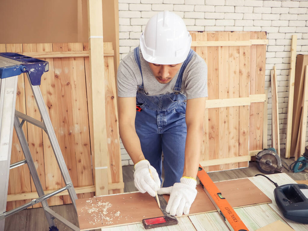 Aziatische jonge timmerman of reparateur met witte helm. werken met hout in binnenwerkplaats. Tekenlijn op houten plank. - Foto, afbeelding