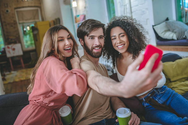 Guy with smartphone taking selfie with two girls indoors. - Foto, imagen