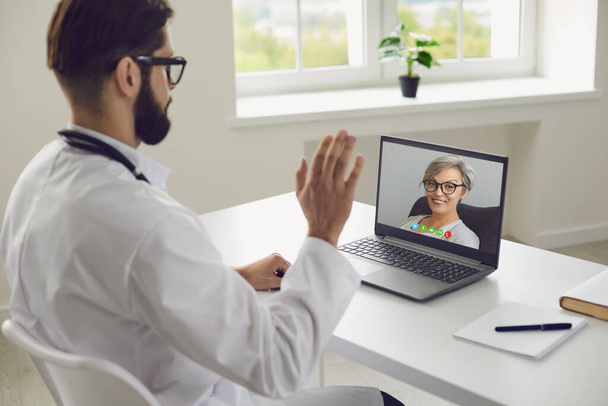 Médico online. Paciente sênior diz sintomas de doença ao médico usando laptop vídeo chat consulta clínica virtual
. - Foto, Imagem