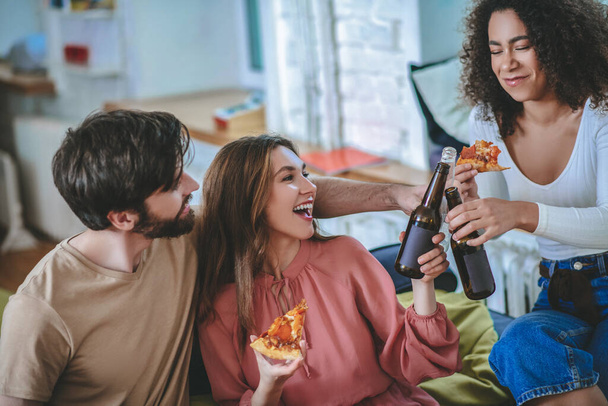 Two girls with pizza and guy holding out bottles towards each other - Photo, image