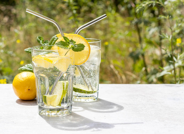 The concept of a summer refreshing drink from limes and lemons with mint. Cold lemonade is a great drink to quench your thirst. With a green garden background and copy space.  - 写真・画像