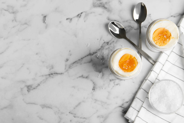 Tasty medium boiled eggs in ceramic holders on white marble table, flat lay. Space for text - Foto, Imagen