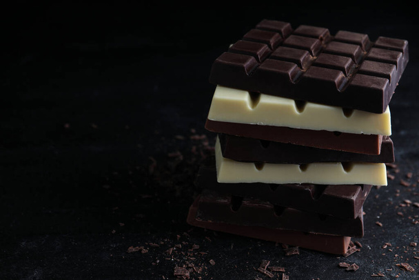 Different tasty chocolate bars on black table. Space for text - Фото, изображение