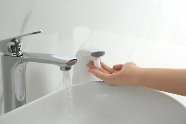 Woman using automatic soap dispenser in bathroom, closeup - Foto, immagini