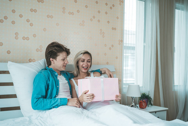 Poikaystävä yllättää tyttöystävänsä lahjapakkauksella sängyllä - Valokuva, kuva
