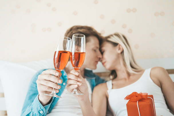 Ευτυχισμένο ζευγάρι πίνει κρασί στην κρεβατοκάμαρα. - Φωτογραφία, εικόνα