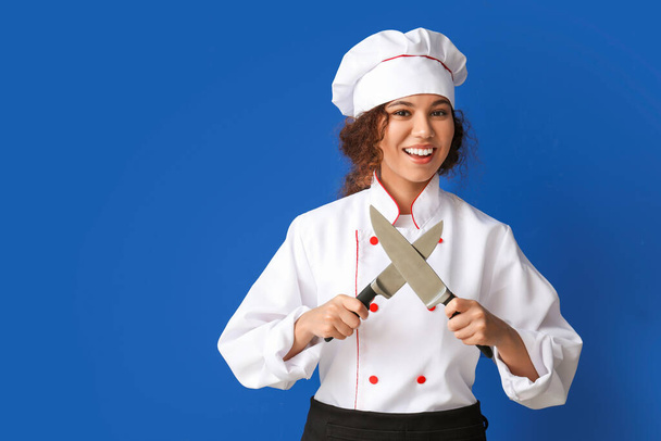 Vrouwelijke Afro-Amerikaanse chef-kok met messen op kleur achtergrond - Foto, afbeelding