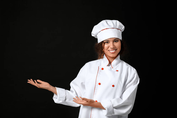 Female African-American chef showing something on dark background - Photo, Image