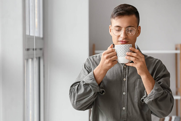 Bello giovane che beve tè vicino alla finestra a casa - Foto, immagini