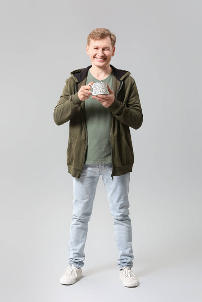 Knappe man met kopje thee op grijze achtergrond - Foto, afbeelding