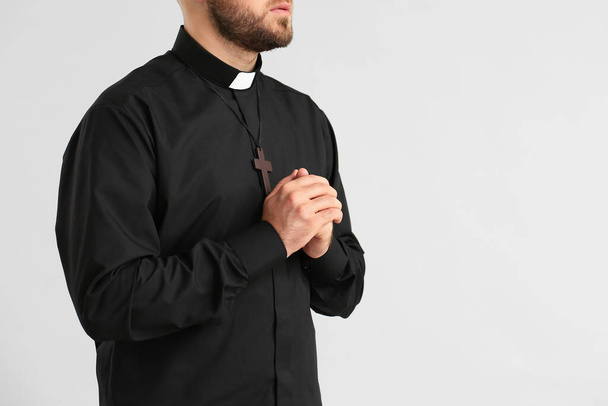 Young priest praying to God on light background - Foto, immagini