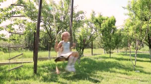 Little girl swinging. little cute girl in a green garden swings on a swing. Slow motion - Πλάνα, βίντεο