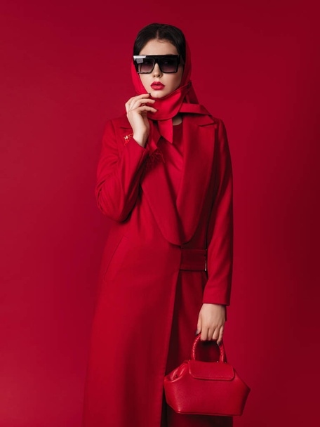 Mode-Modell in roten Kleiden.Taillieren Sie das Porträt eines attraktiven Modells mit hellem Make-up, das in die Kamera schaut. Sie trägt einen roten Mantel und eine Handtasche. model.roter Lippenstift - Foto, Bild