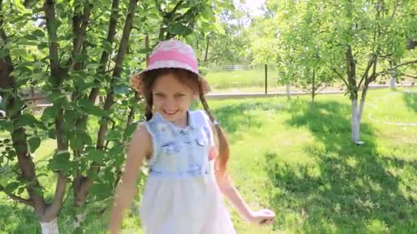 Little cute girl dressed in a dress and a hat laughs in a green summer garden. baby laughter, smile. happiness of the child - Metraje, vídeo