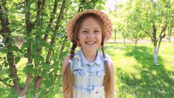Little cute girl dressed in a dress and a hat laughs in a green summer garden. baby laughter, smile. happiness of the child - Video, Çekim