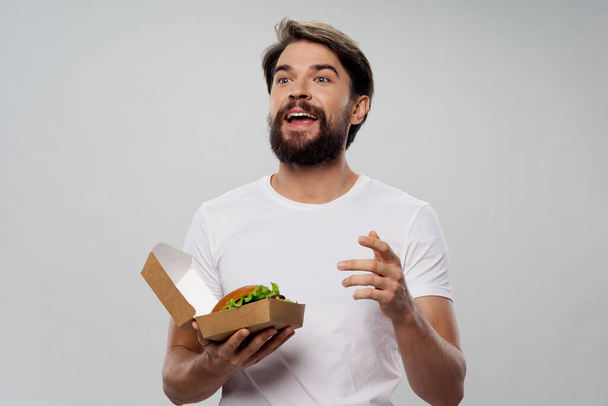 ハンバーガーを持った感情的な男が手でジェスチャーしてる  - 写真・画像