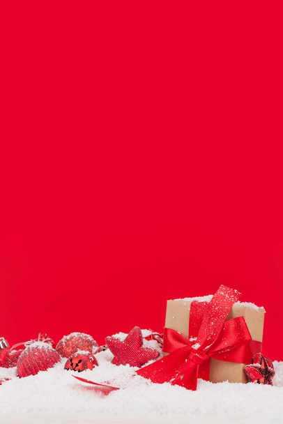Weihnachtsgrußkarte mit Dekor und Geschenkschachtel im Schnee auf rotem Hintergrund und Kopierplatz für Ihre Weihnachtsgrüße - Foto, Bild