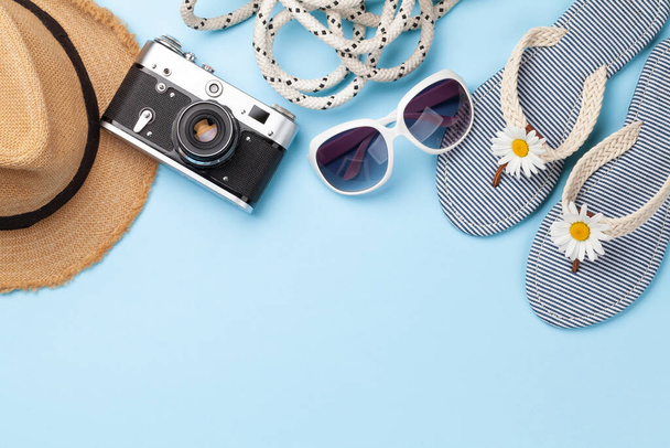 Articles et accessoires de vacances d'été. Tongs, lunettes de soleil, appareil photo et chapeau de soleil sur fond bleu. Vue du dessus plat avec espace de copie - Photo, image