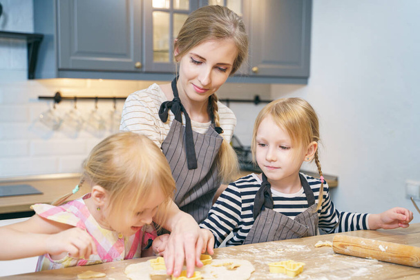 Happy family young mother and two little daughters preparing dough for cookies together in the kitchen. - Photo, image