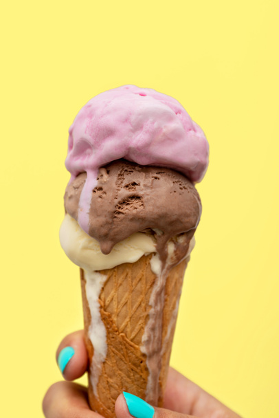 Woman's hand holding an ice cream cone melting in a yellow background - Photo, Image
