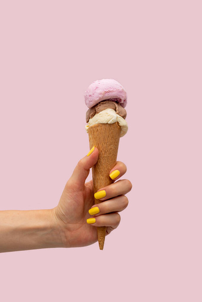 Γυναικείο χέρι που κρατάει παγωτό πάνω από ροζ φόντο - Φωτογραφία, εικόνα