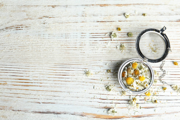 Dry chamomile flowers in infuser on white wooden table, flat lay. Space for text - 写真・画像