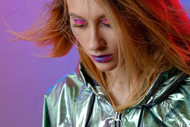 Beautiful girl with bright makeup in a metallic color windbreaker posing on a trendy pink neon background. - Foto, afbeelding