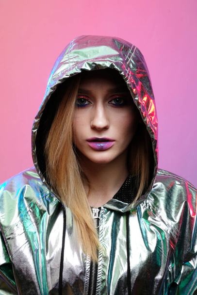 Beautiful girl with bright makeup in a metallic color windbreaker posing on a trendy pink neon background. - Valokuva, kuva