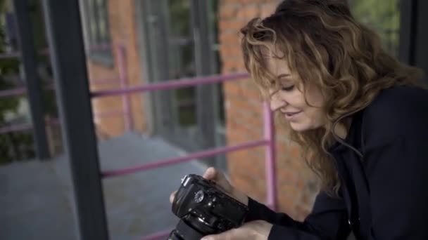 Πορτραίτο γυναίκας φωτογράφου με επαγγελματική κάμερα. Πάμε. Πλευρική άποψη της καυκασίας γυναίκα με σγουρά μαλλιά λήψη φωτογραφιών στην κάμερά της σε φόντο κόκκινο τούβλο τοίχο. - Πλάνα, βίντεο