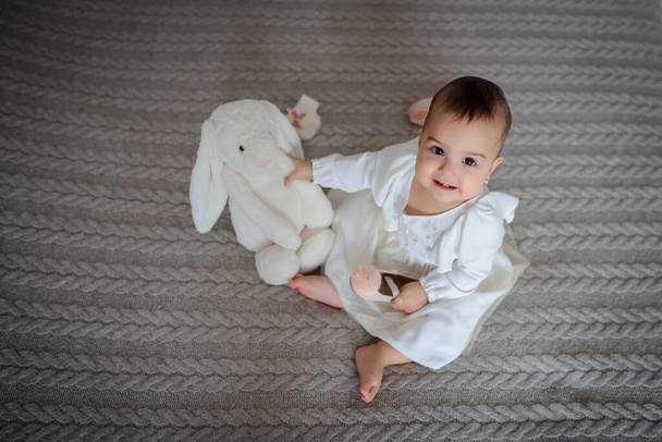 vue du haut d'une jolie petite fille en robe blanche sur une couverture grise à la maison avec un lapin à côté d'elle - Photo, image