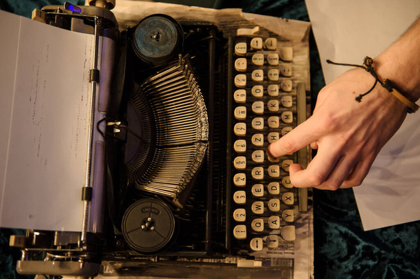 вид зверху руки людини, що друкує на старовинній друкарській машинці на шматочку газети і темно-синій оксамитовій тканині на підлозі
  - Фото, зображення