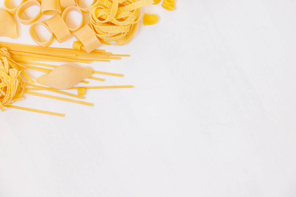 Verschiedene rohe Nudeln auf weißem Holzgrund. Ansicht von oben. Italienische Pasta für Restaurant mit Platz für Text. - Foto, Bild