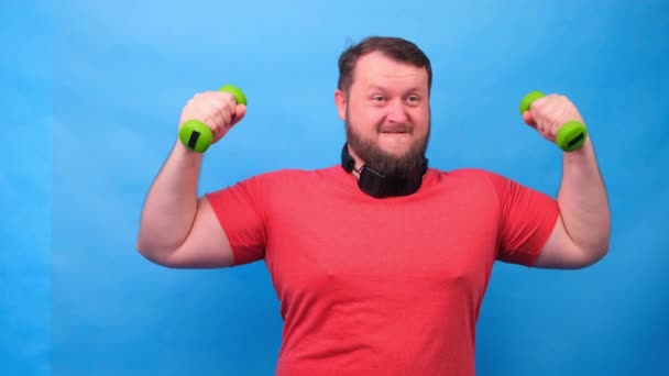 fetter schicker Mann in rosa T-Shirt mit Hanteln, witzig bei Übungen auf blauem Hintergrund. - Filmmaterial, Video