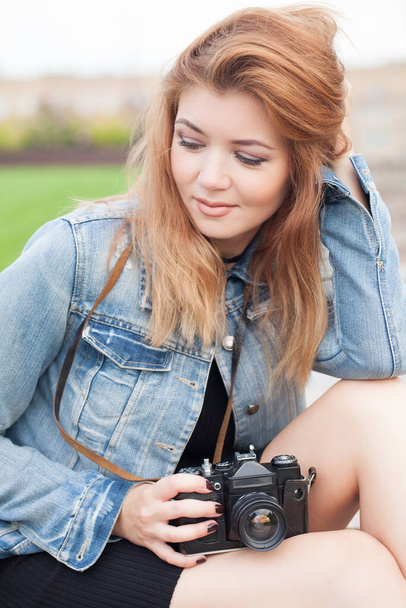 Młoda fotograf dziewczyna spaceruje ulicą w dżinsach kurtka ze starym aparatem - Zdjęcie, obraz